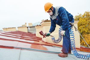 roofer builder worker with pulverizer spraying paint on metal sheet roof